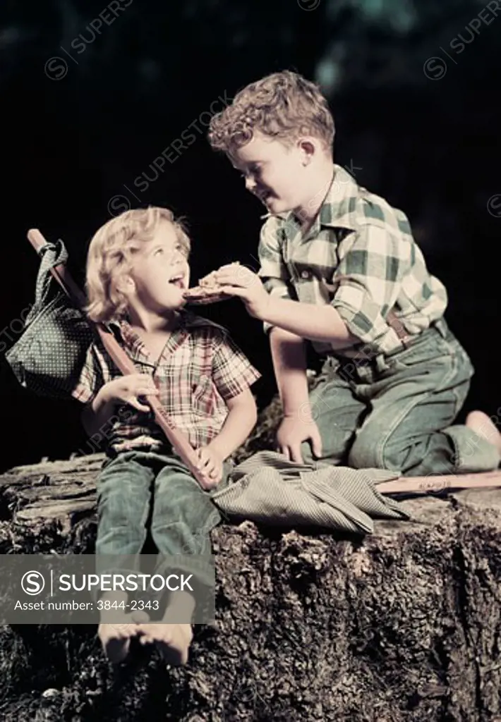 Side profile of a boy feeding a girl sitting on a rock