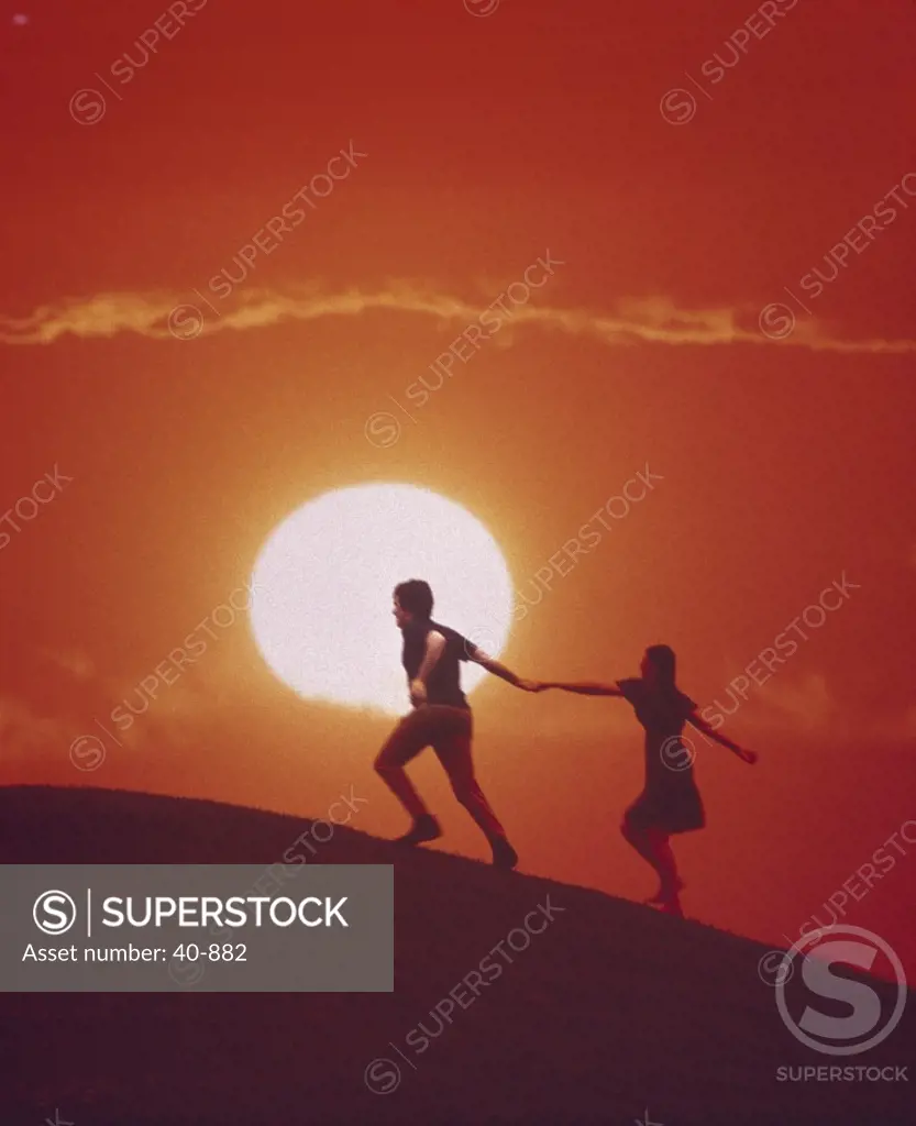 Couple holding hands with setting sun behind