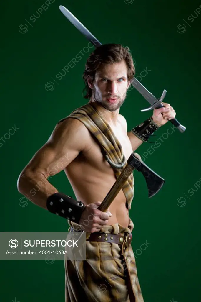 Young man in warrior costume holding a sword and an axe