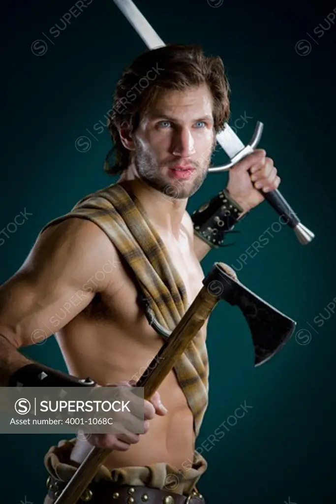 Young man in warrior costume holding a sword and an axe