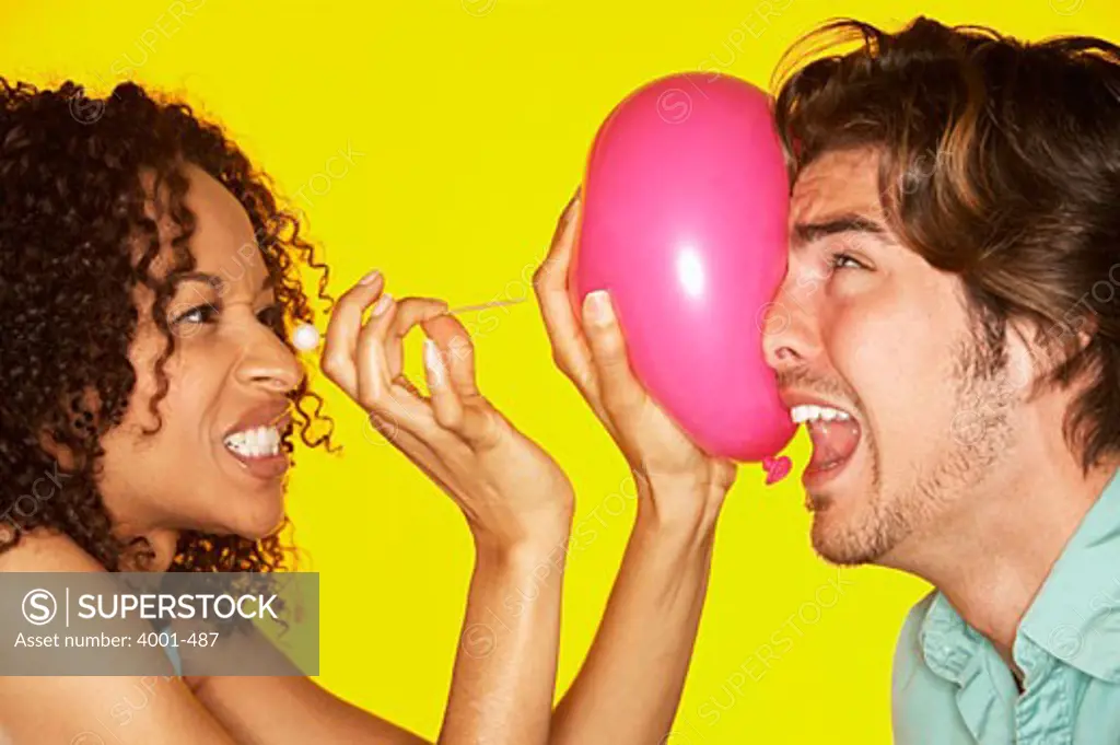 Young woman popping a balloon on a man's face with a pin