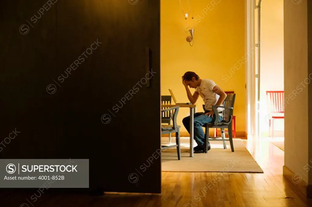 Young man using a laptop in his house and looking sad