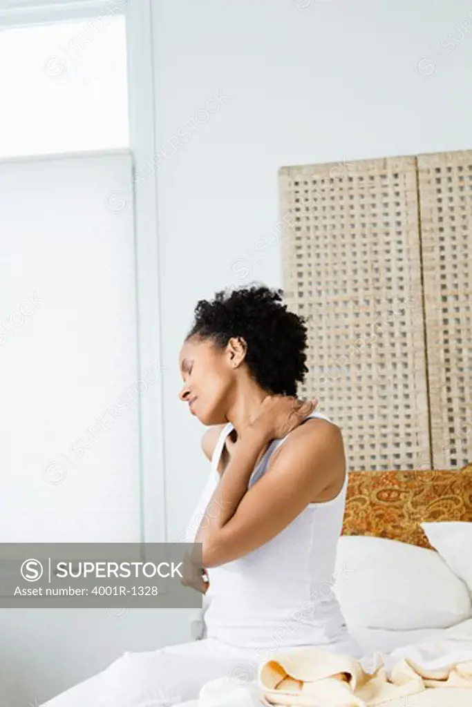 Mid adult woman sitting on the bed and suffering from backache