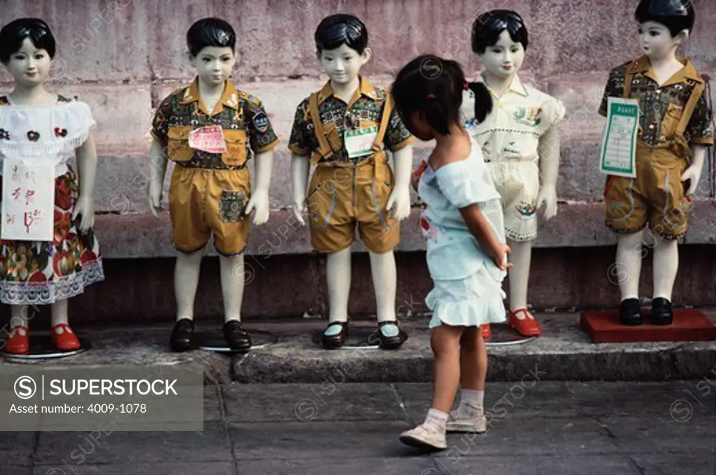 Girl browsing the clothes for sale on the life-size mannequins of children on street, China