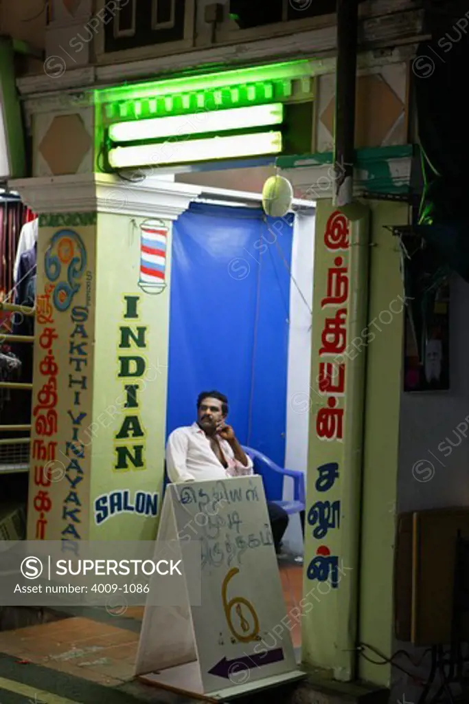 Man sitting outside of the door of a salon, Little India, Singapore