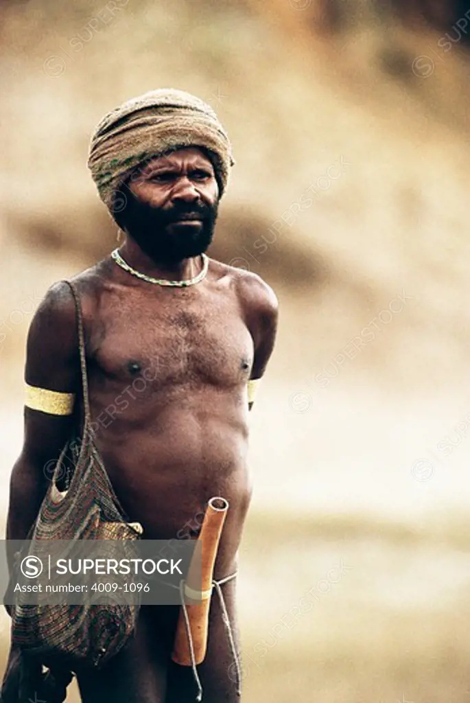 Indigenous man wearing a turban and carrying a knit bag over his shoulder and with a gourd tied to his waist, Irian Jaya, New Guinea, Indonesia