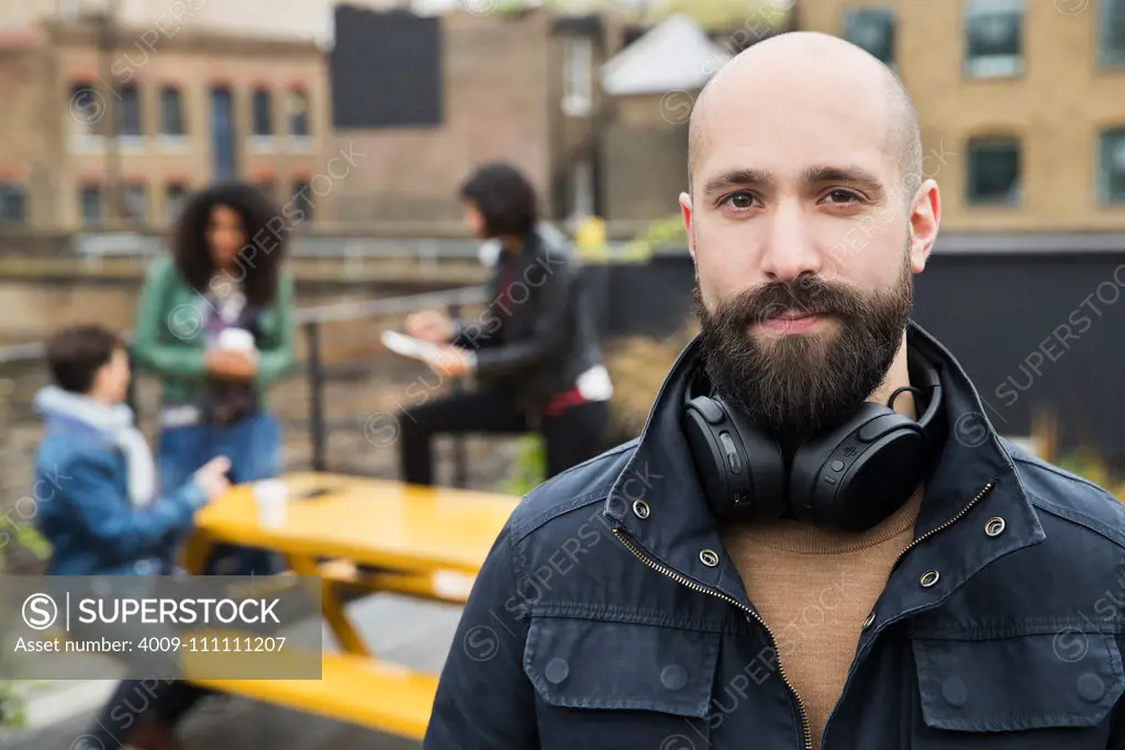Portrait of man with group of friends working on tablets at outdoor patio table in co-working space in the background