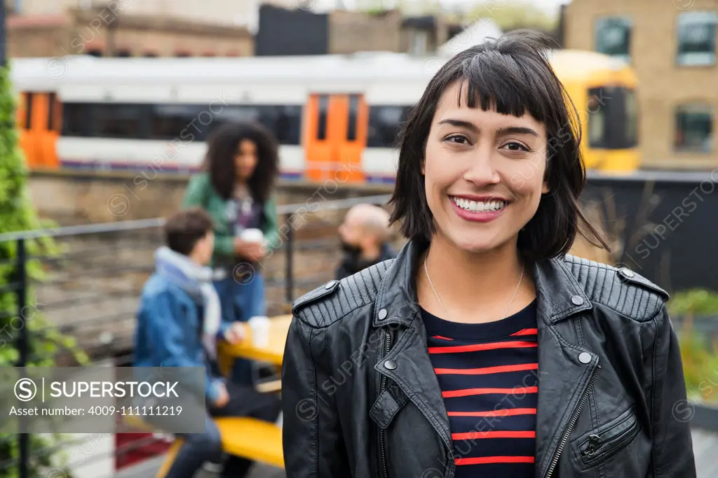 Portrait of Woman with group of friends working on tablets at outdoor patio table in co-working space in the background