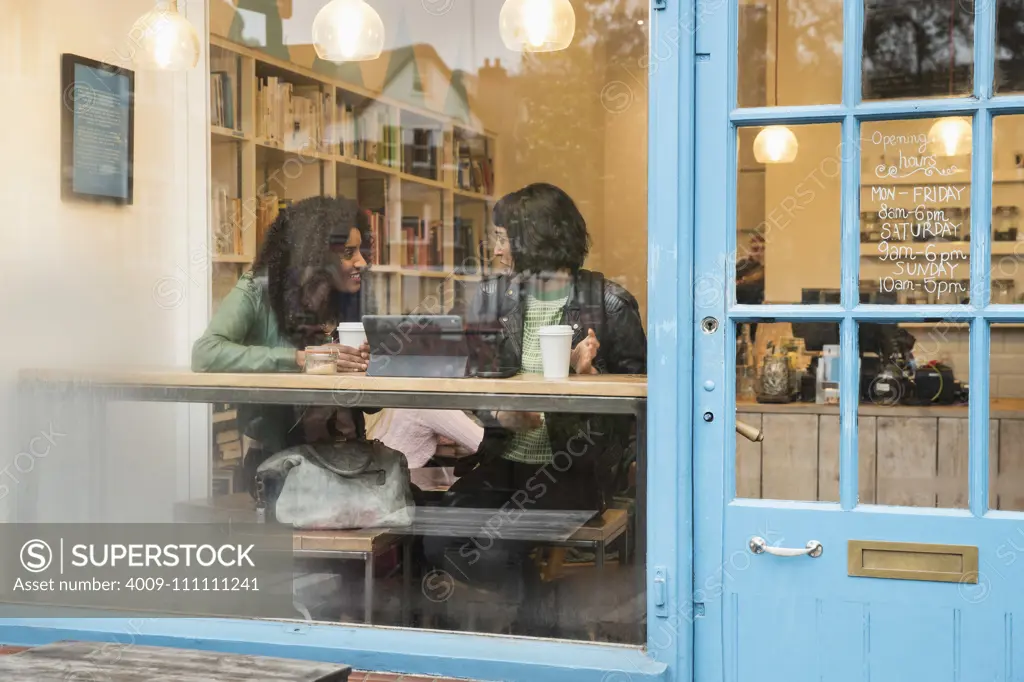 Two women sitting in window of cafe looking at tablet