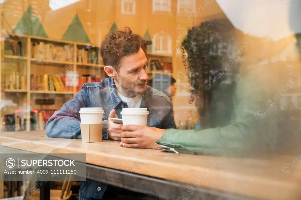 Friends sitting in window of cafe with mobile phone