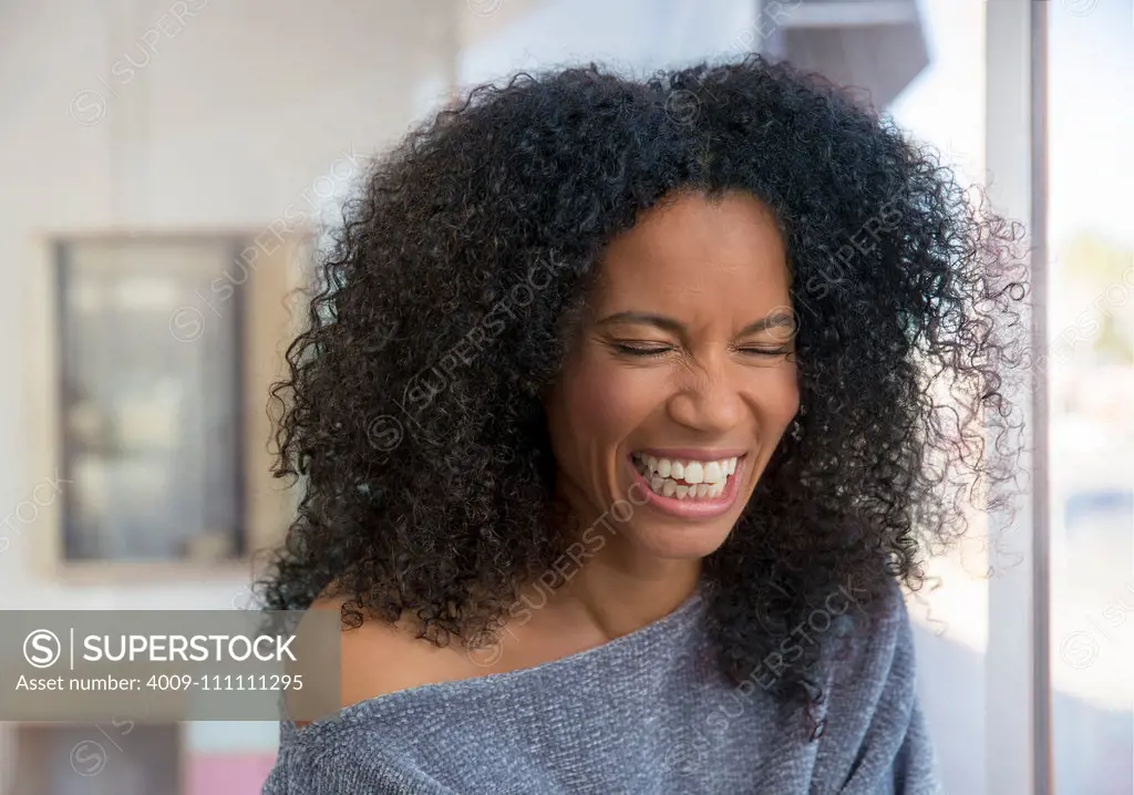 Mixed race, middle-aged woman laughing in a brightly lit room.