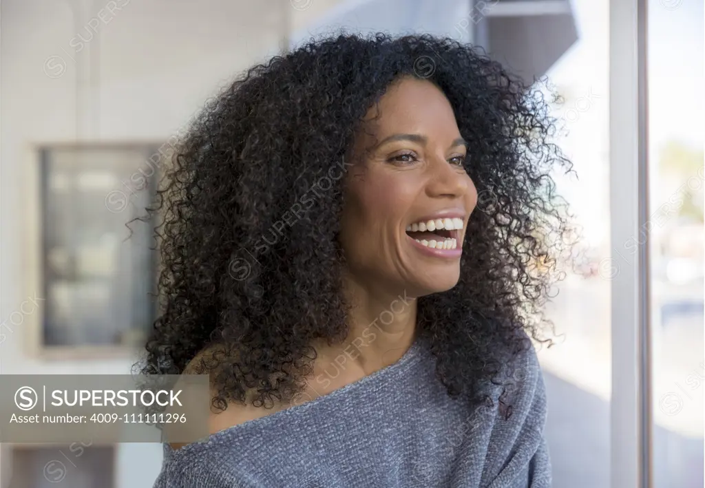 Mixed race, middle-aged woman laughing and looking out the window.