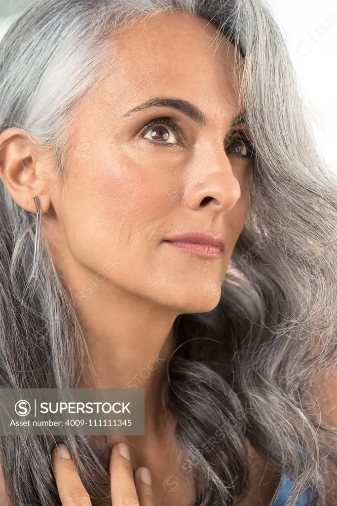 Close up of a middle-aged woman with gray hair, looking up off camera and brushing away her hair.