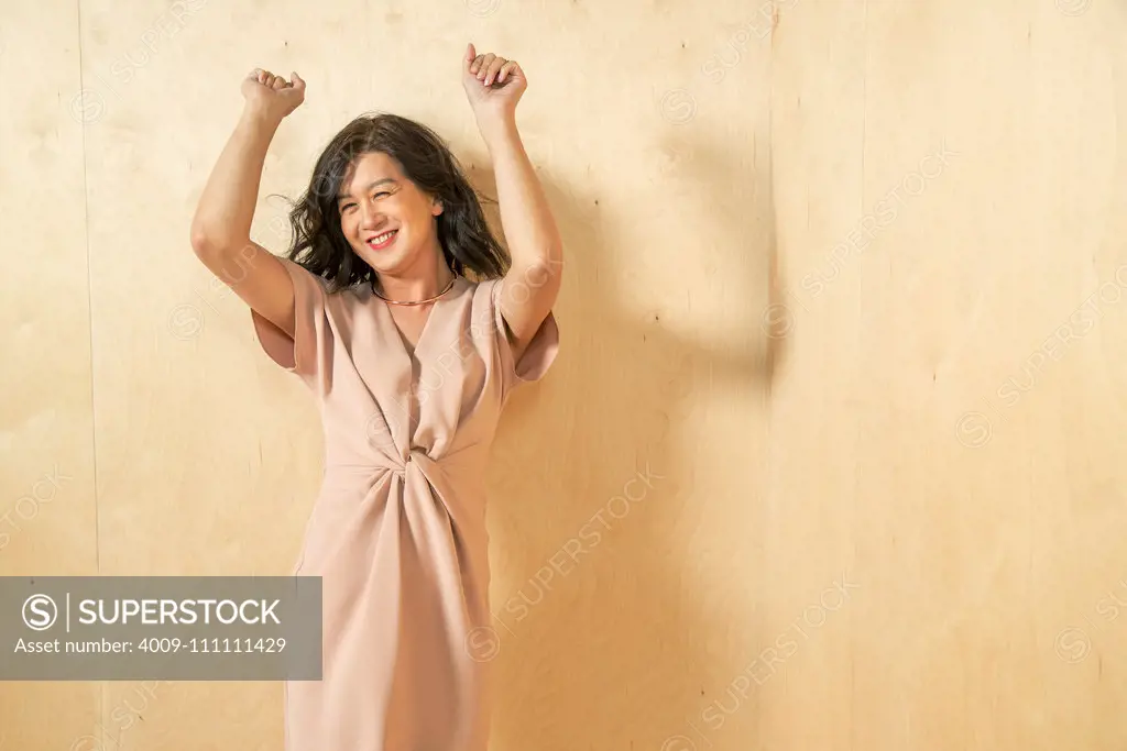 A woman holds her hands up, dancing, against a wood paneled wall.