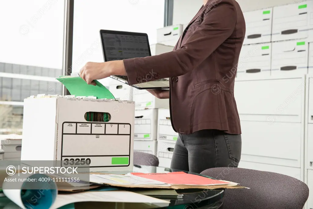 Tight shot of a woman holding a laptop sorting through a box.