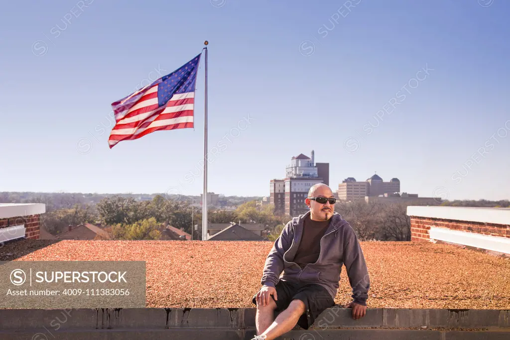 Smiling man sitting on rooftop near American flag
