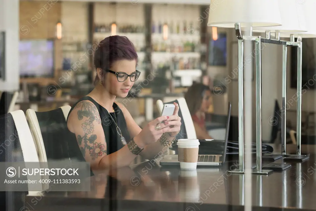 Caucasian woman using cell phone and laptop in coffee shop