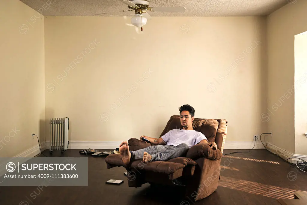 Man sitting in armchair watching television in barren apartment