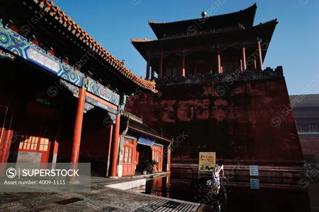Man riding a bicycle through a pool of water in front of an ancient Chinese building, Forbidden City, Beijing, China