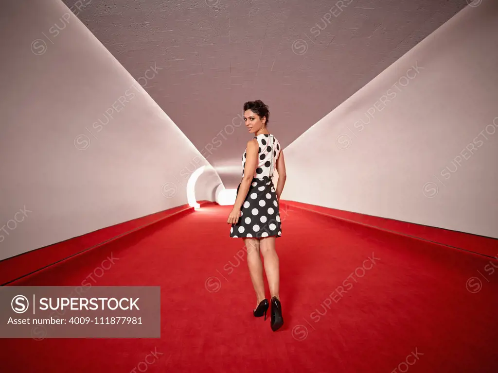 Full length portrait of a woman walking down a hallway with red carpet at the TWA hotel designed by Eero Saarinen at JFK Airport