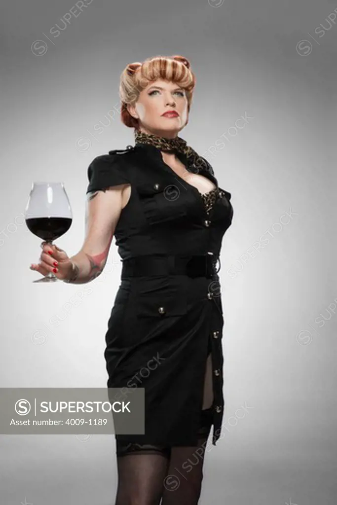 Portrait of tattooed pin-up girl, holding large glass of red wine