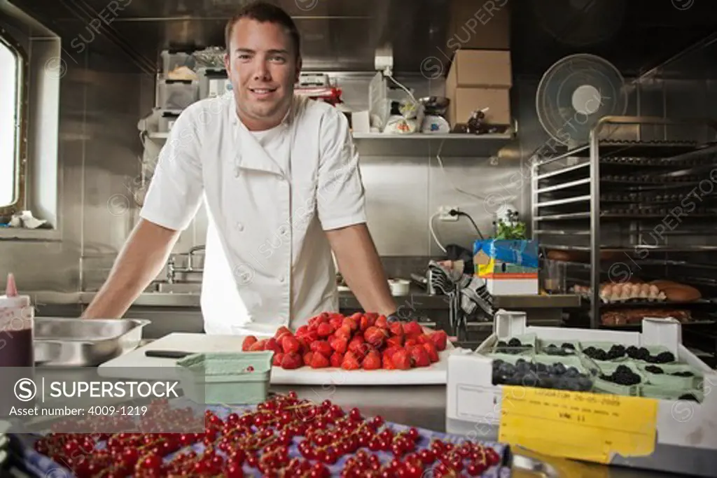 Pastry chef leaning on kitchen counter with assorted berries being prepped on counter