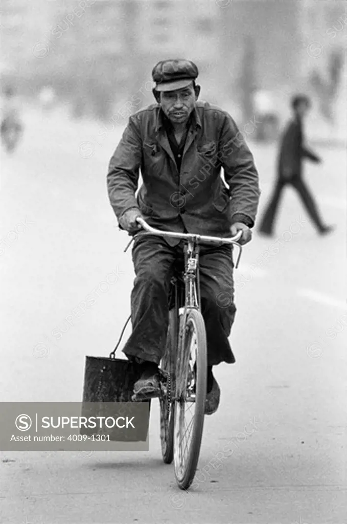 China, Datong, Man riding bike carrying bucket