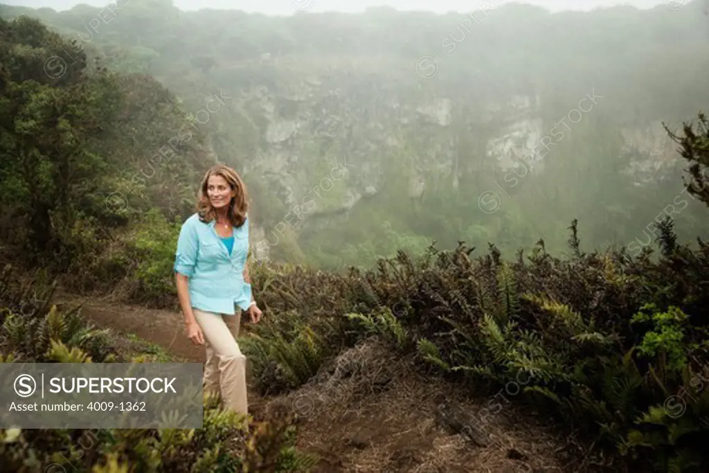 Ecuador, Galapagos Islands, Woman walking on trail along lush mountain edge