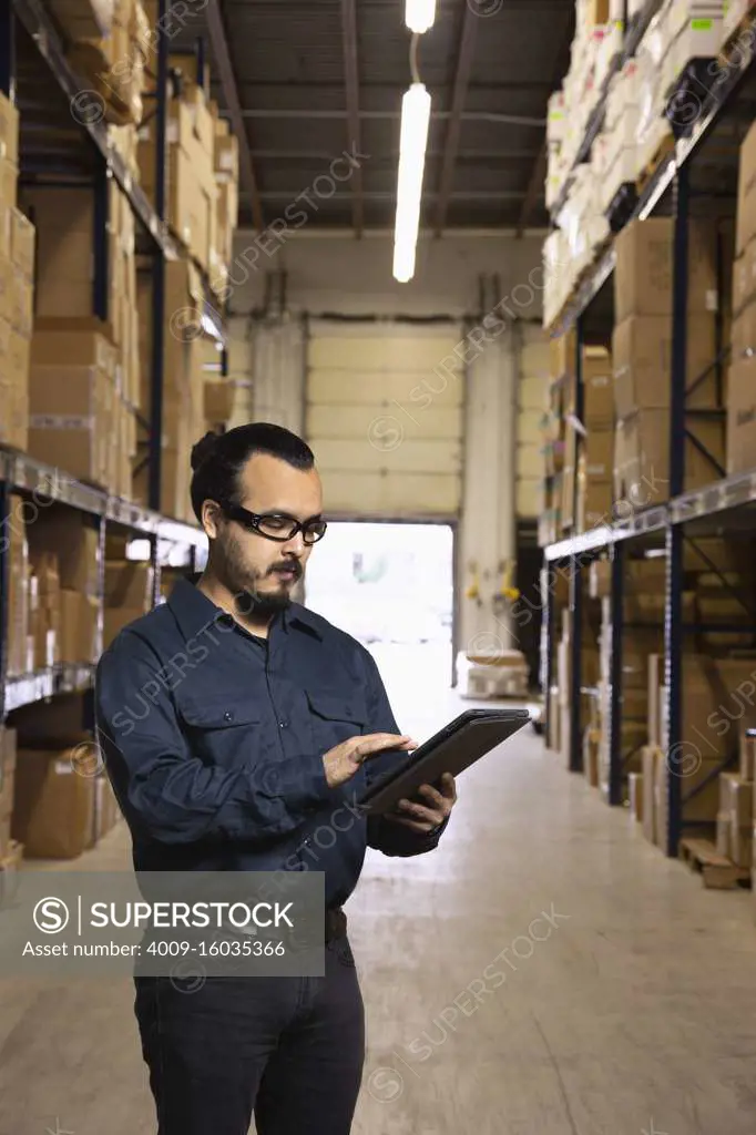 Young hispanic warehouse working typing into tablet