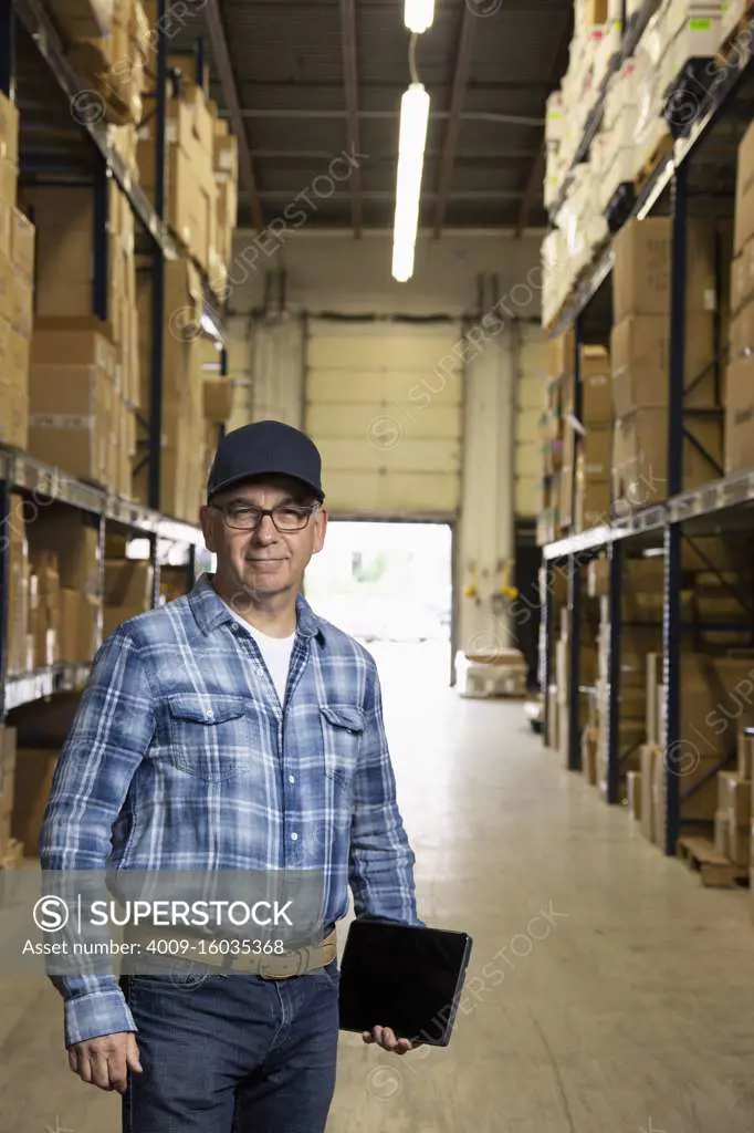 Middle aged warehouse worker smiling at camera holding a tablet