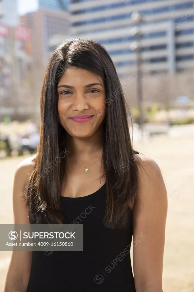 Smiling portrait of young ethnic woman standing in park wearing black tank top 