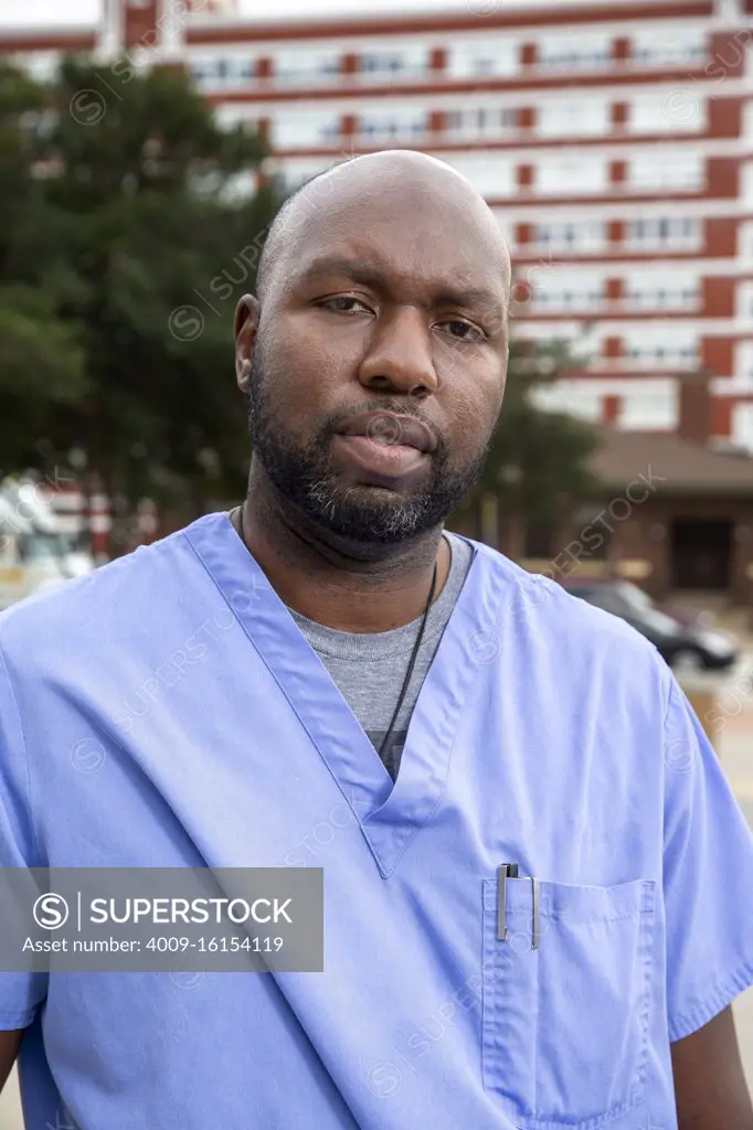 Portrait of middle aged man  with beard and a bald head wearing scrubs standing outside looking at camera