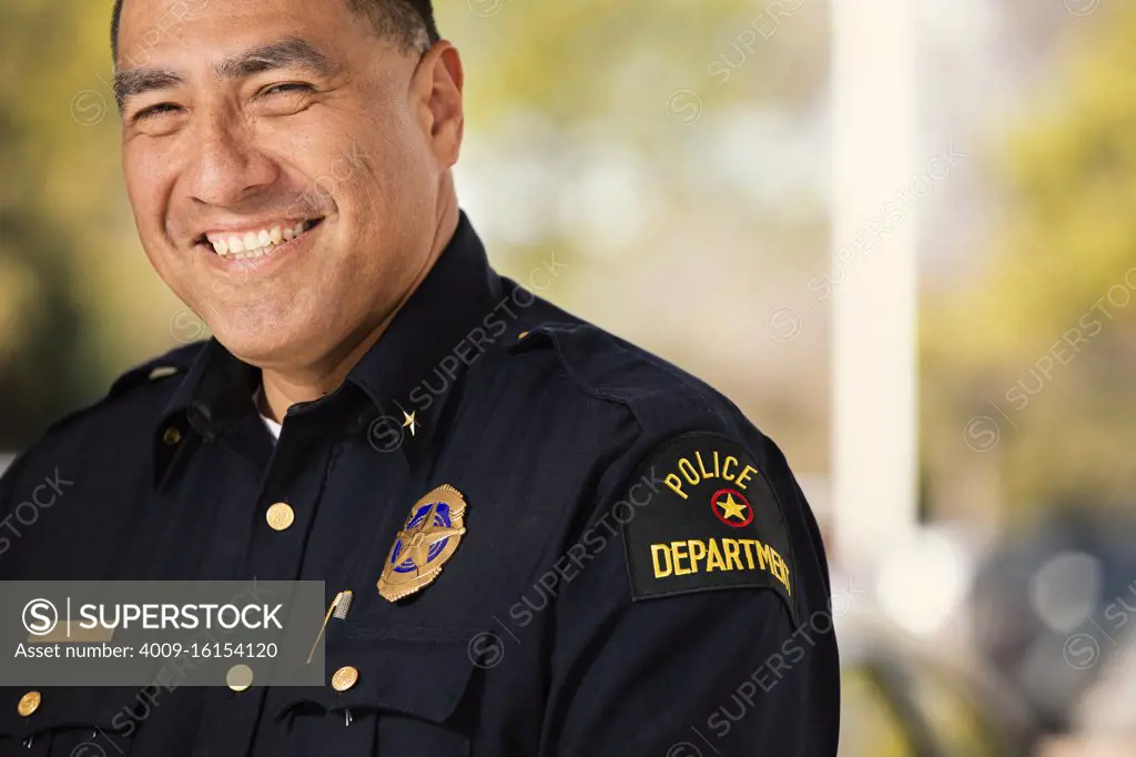 Portrait of Police officer standing outside with arms crossed looking towards camera smiling 
