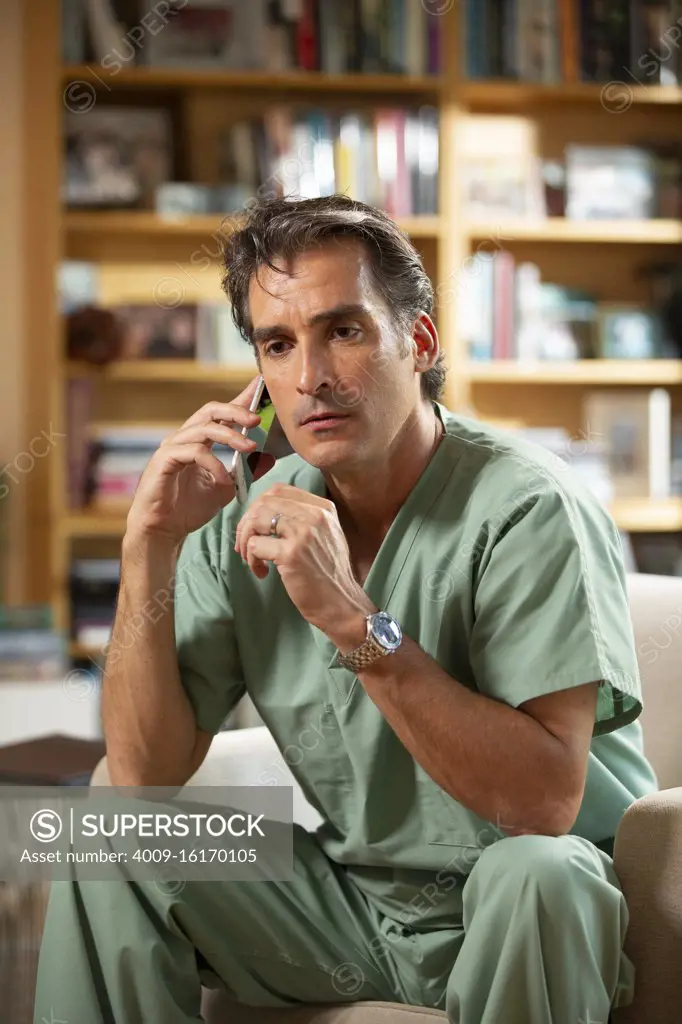 Hispanic Male doctor practicing tele-medicine from his home office, Talking to patient on cell phone 