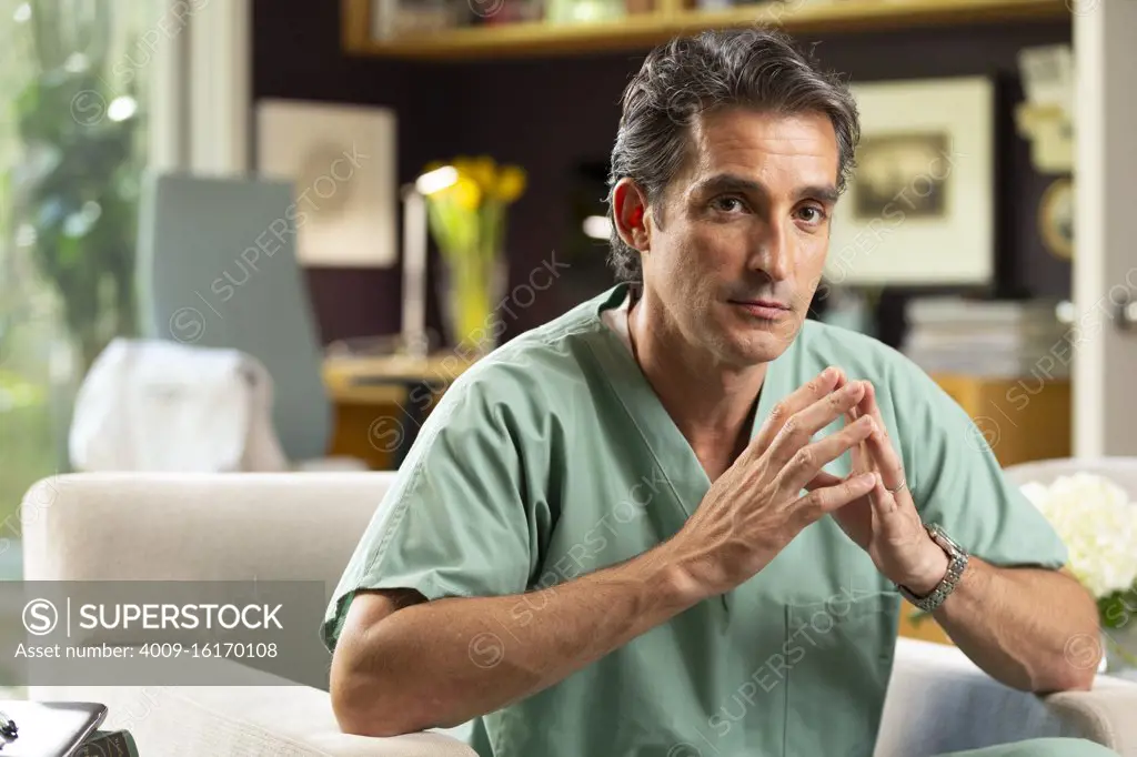 Portrait of Hispanic Male doctor sitting in his home office, taking a break from practicing Tele-medicine 