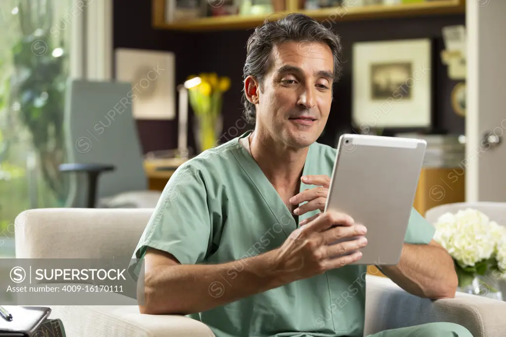 Hispanic Male doctor practicing tele-medicine from his home office, Talking to patient via video call on tablet 