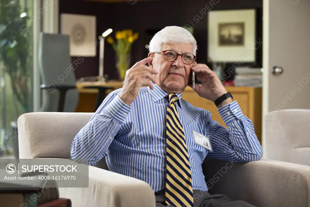 Senior Caucasian doctor practicing tele-medicine from his home office, Talking to patient on telephone