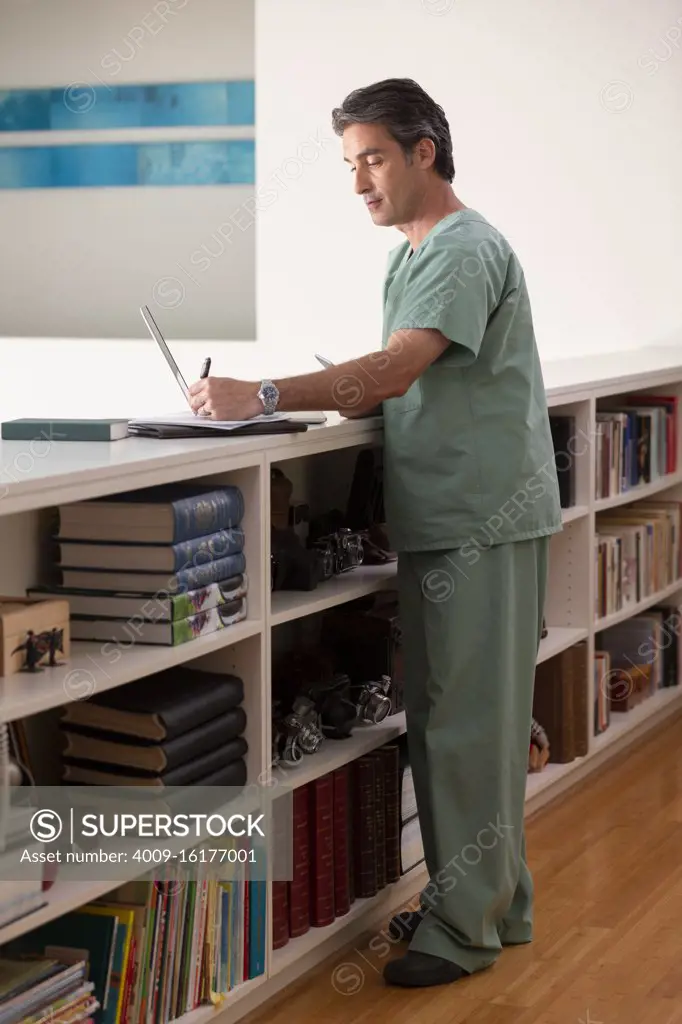 Hispanic Male doctor in his home practicing Telemedicine taking notes 