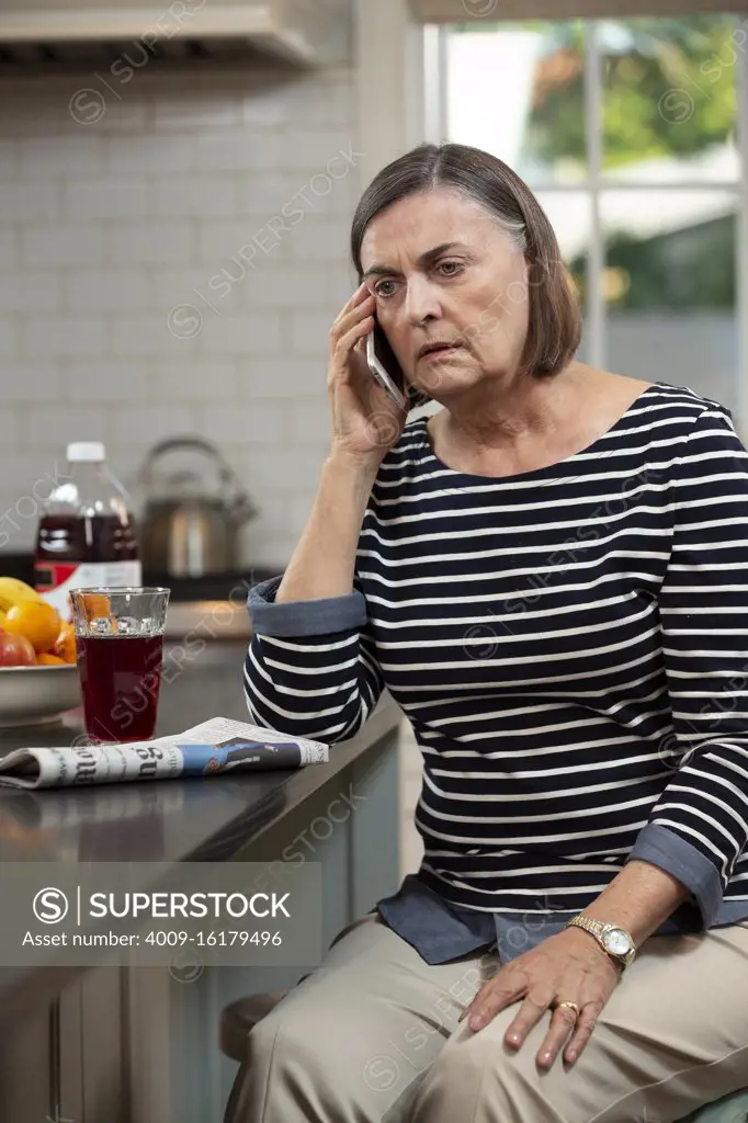 Senior Caucasian woman looking worried on the phone in her kitchen
