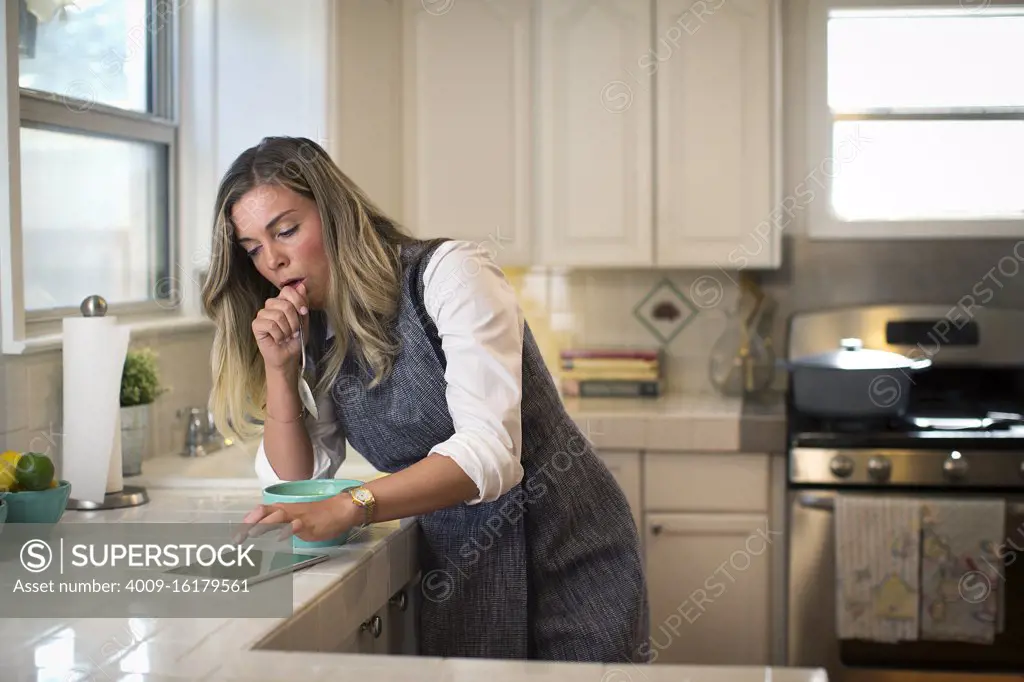 Coughing young woman in her kitchen, eating breakfast getting on her iPad 