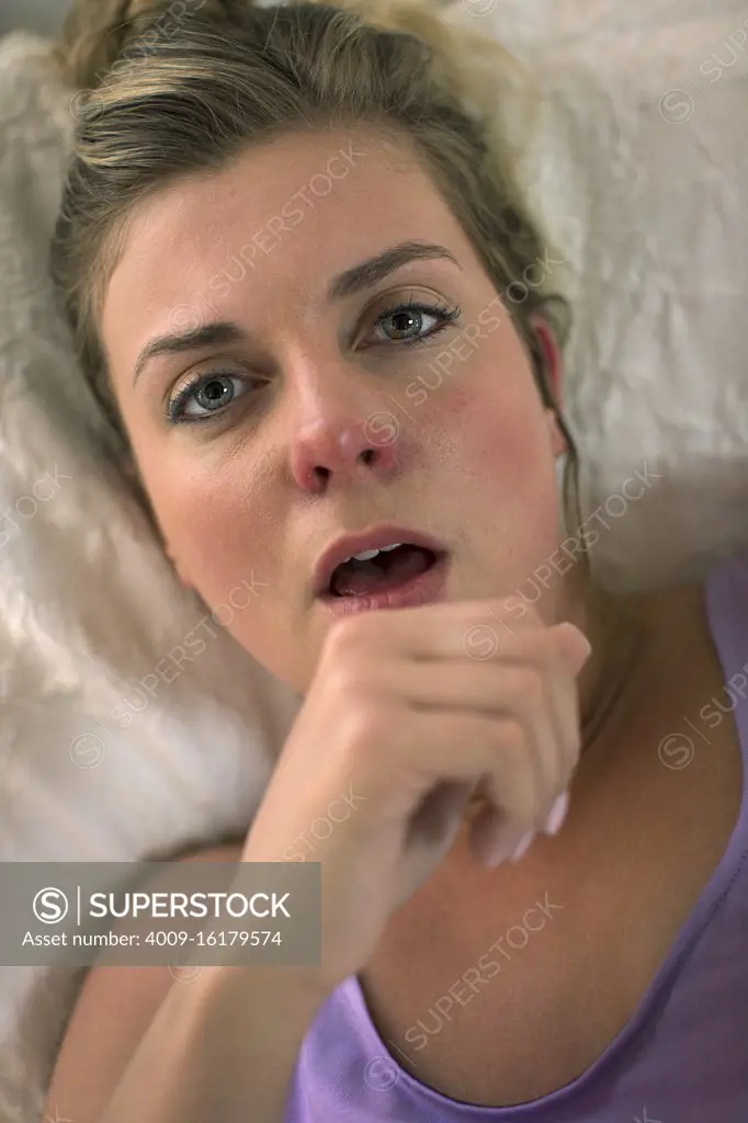 Coughing young woman in her bed with using smartphone to check in with doctor, doctors view of patient on video call