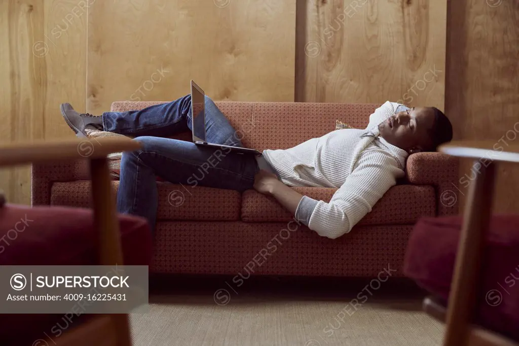 Young man taking a nap on loveseat with his computer on his lap