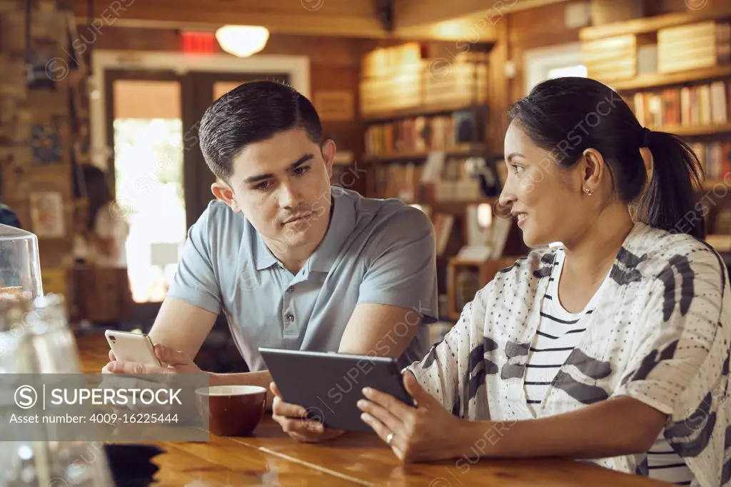 Young man and woman sitting at counter in cafe bookstore looking at tablet 