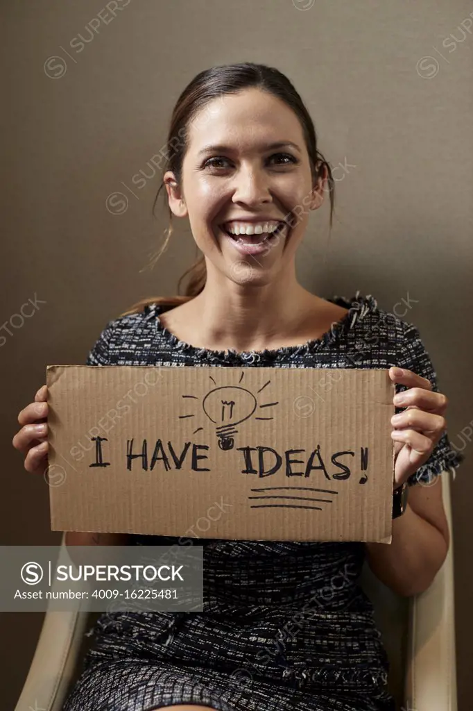 Portrait of Young woman sitting in chair holding cardboard sign the reads ÒI have Ideas, looking off camera 