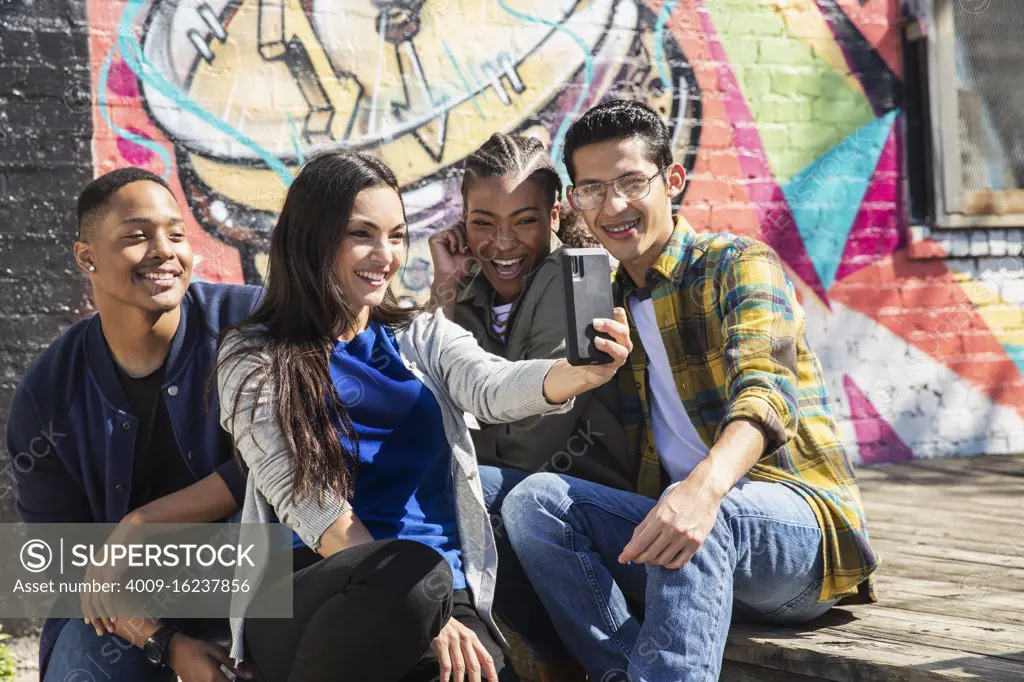 Group of young co-workers hanging out in front of graffitied wall taking selfie with mobile phone 