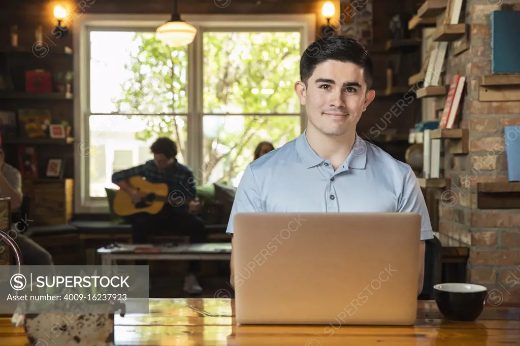 Portrait of young man sitting at table in coffee shop bookstore using laptop computer 