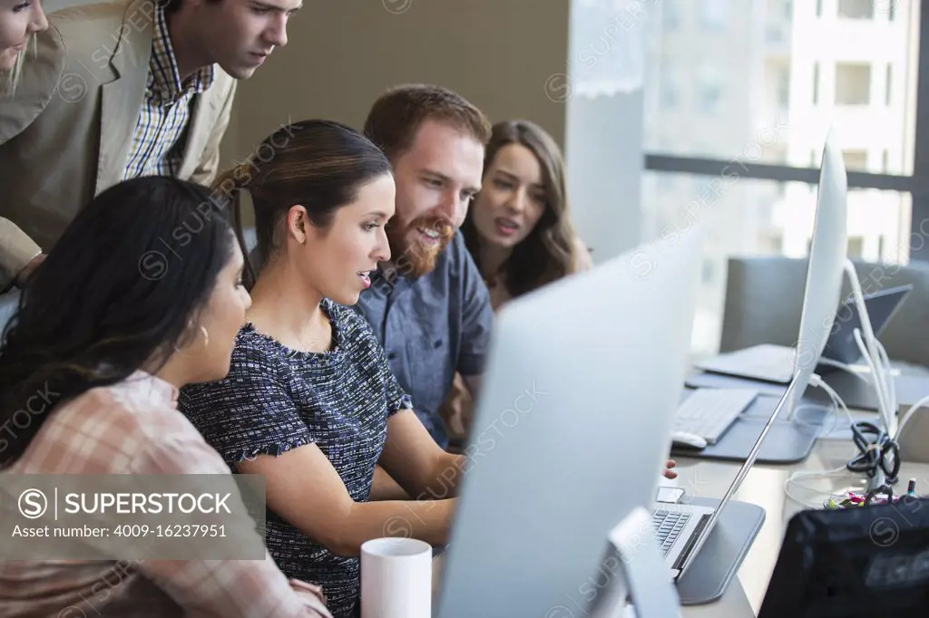 Young woman using laptop computer in conference room showing co-workers something on screen 