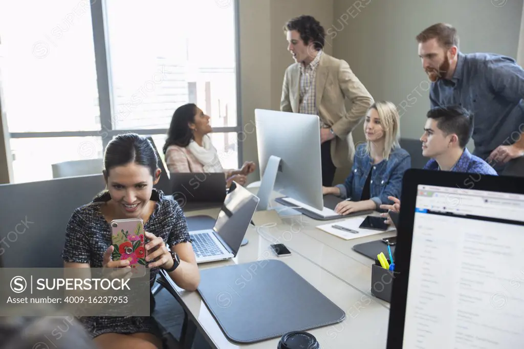 Woman taking picture with mobile phone, while colleagues work in background of conference room 