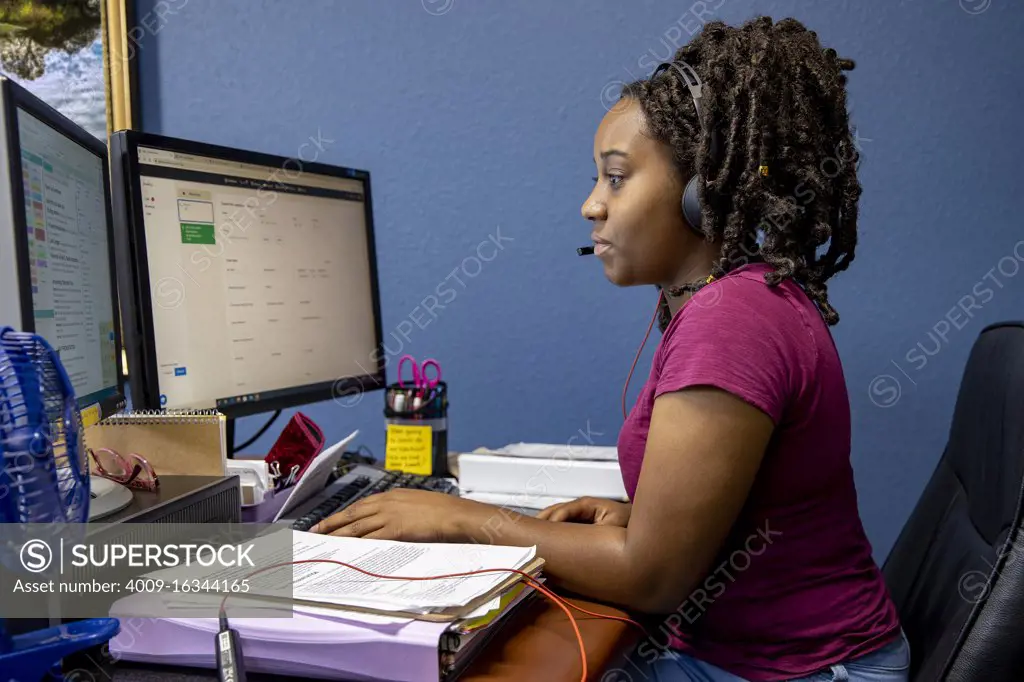 A portrait of an African American woman at her call center desk and her headset on, working from home.