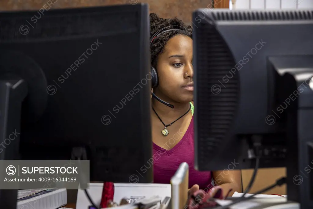 A portrait of an African American woman at her call center desk and her headset on focusing on her computer monitor.